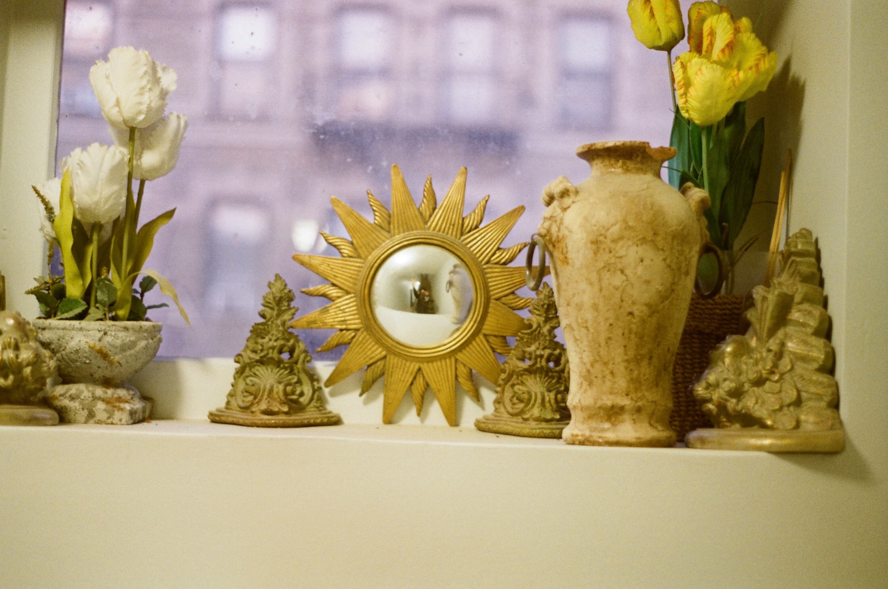 A still life on a windowsill in New York — a sunburst mirror catches the room